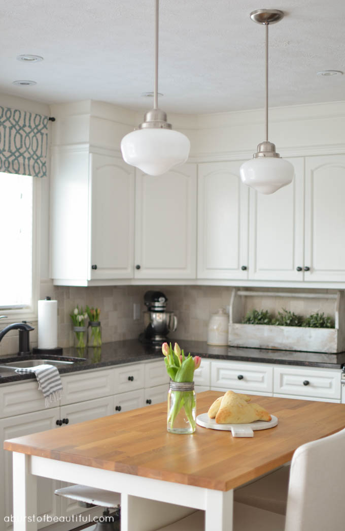 Beautiful white farmhouse kitchen, complete with butch block island, custom cabinetry and schoolhouse pendant lights | A Burst of Beautiful